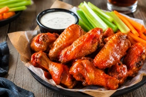 Alitas doradas con salsa roja brillante acompañadas de apio y aderezo